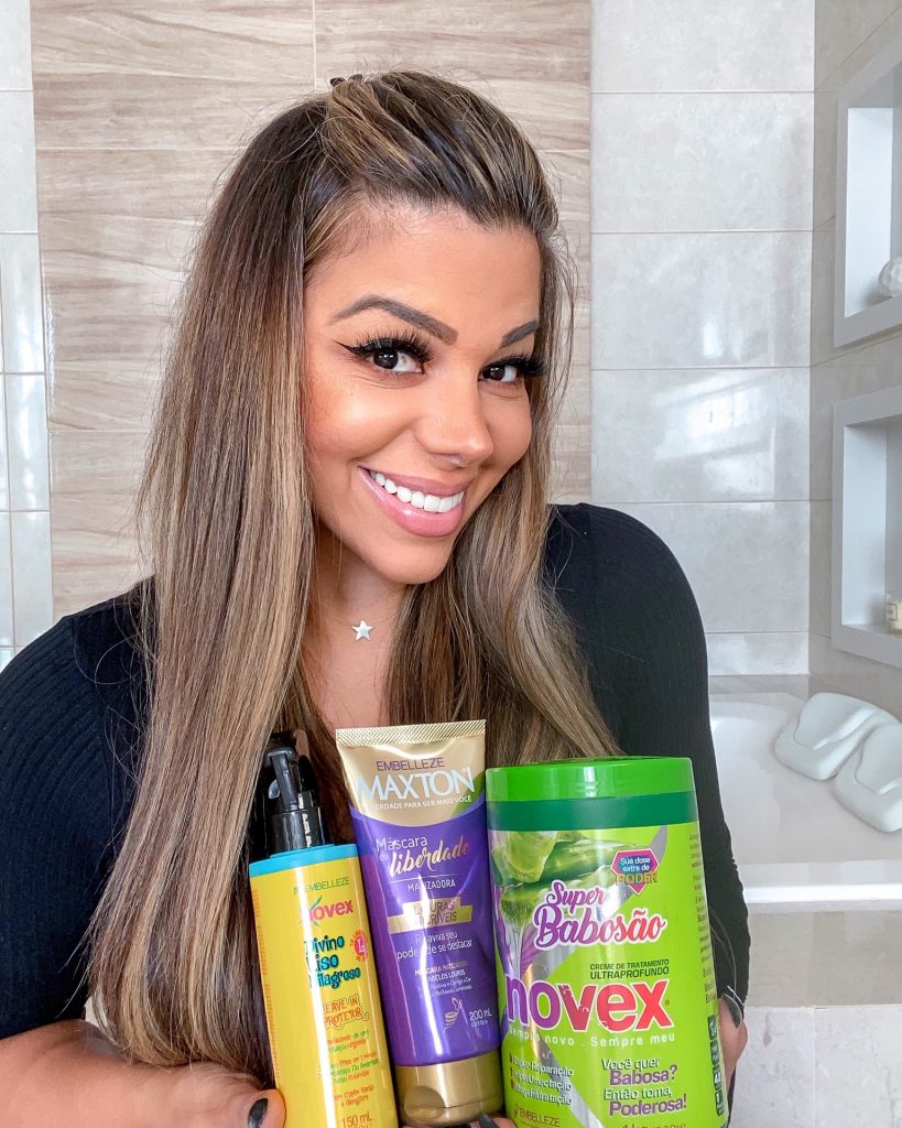 Evelyn Regly segurando três produtos da Embelleze: Leave-in Protetor Divino Liso Milagroso, Maxton Máscara Matizadora e Creme de Tratamento Novex Super Babosão.